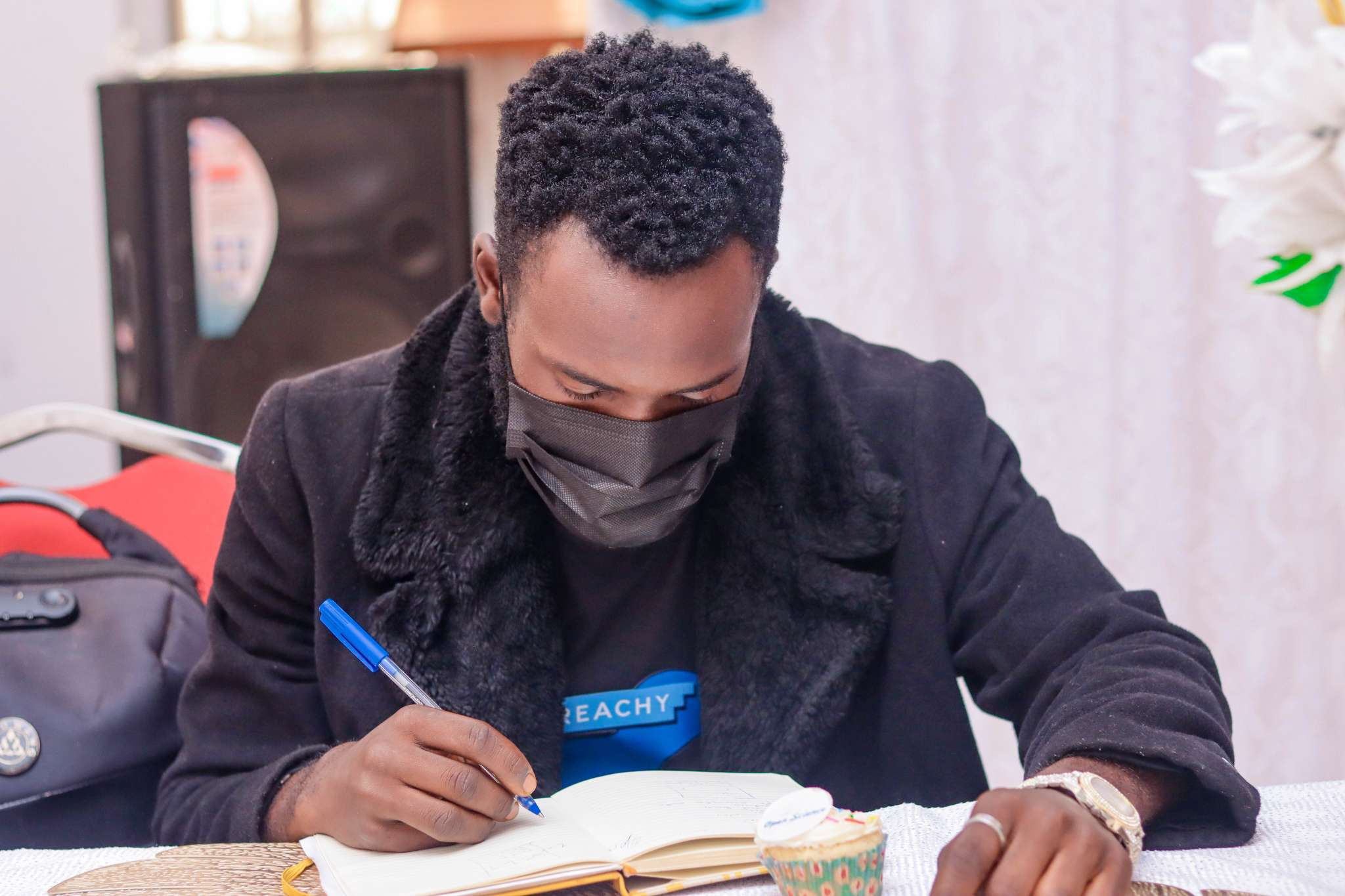 A young black man in the Cameroon 1,000 interns celebration writes down some ideas with pen and paper.